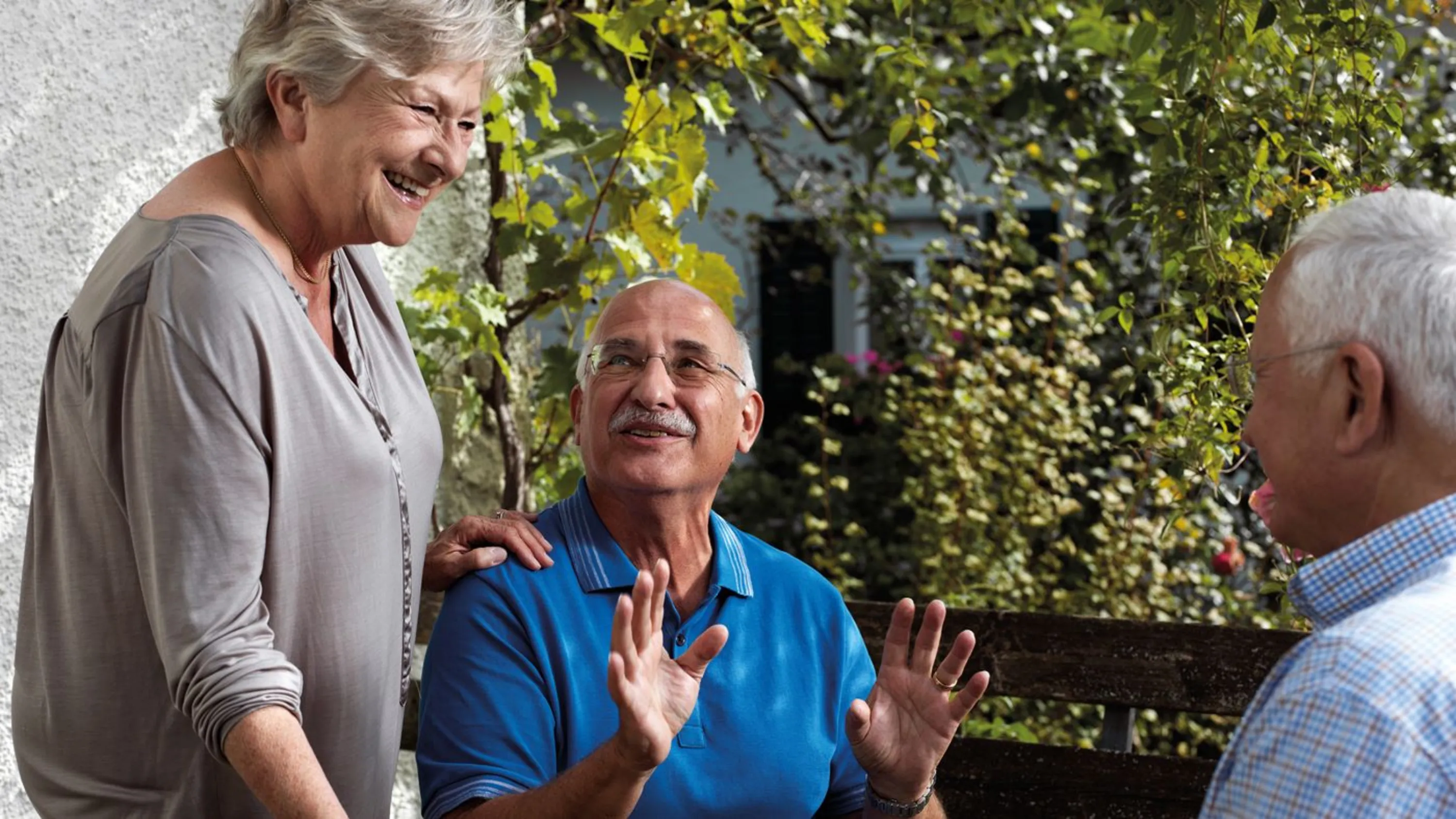 Eine Gruppe älterer Menschen sitzt lachend vor dem Haus.