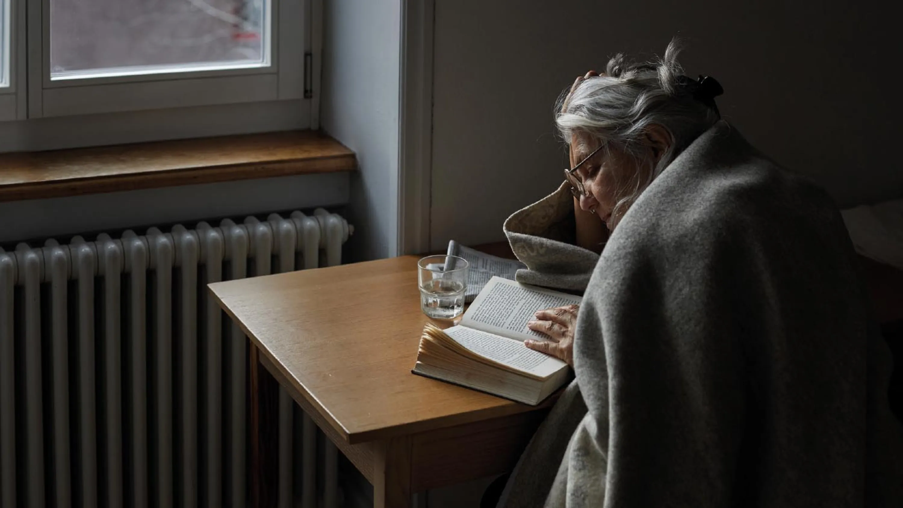 Un anziano con una coperta e un tè legge un libro.