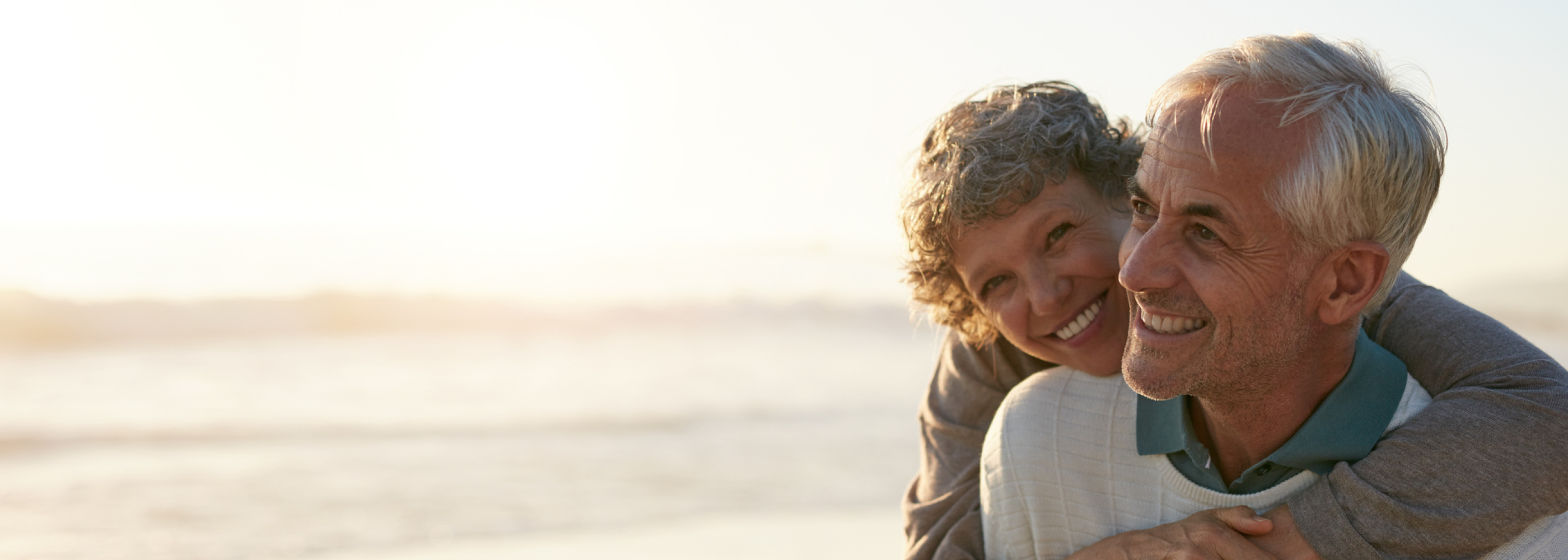 Älteres Paar umarmt sich lachend am Strand.